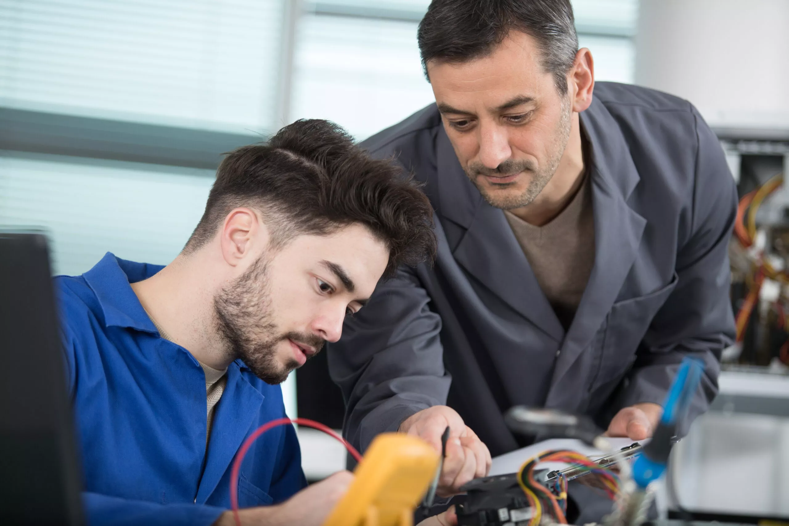 supervisor guiding apprentice using a multimeter